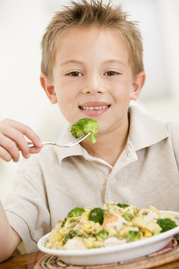 Young boy indoors eating pasta with brocolli smiling. Young boy indoors eating pasta with brocolli smiling