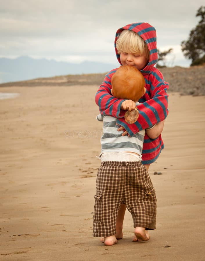 Two young boys one redhead and one blond hugging each other on a beach. Two young boys one redhead and one blond hugging each other on a beach