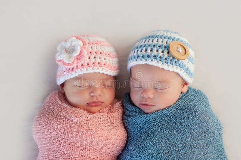 Five week old sleeping boy and girl fraternal twin newborn babies. They are wearing crocheted pink and blue striped hats. Five week old sleeping boy and girl fraternal twin newborn babies. They are wearing crocheted pink and blue striped hats.