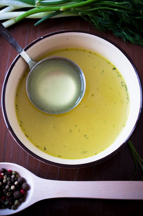 Broth, bouillon, clear soup on the table with spices and herbs and soup ladle. Broth, bouillon, clear soup on the table with spices and herbs and soup ladle