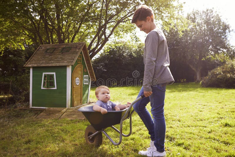 Broer In Garden Wheelbarrow van de jongens de Duwende Baby stock fotografie Broer In Garden Wheelbarrow van de jongens de Duwende Baby stock fotografie