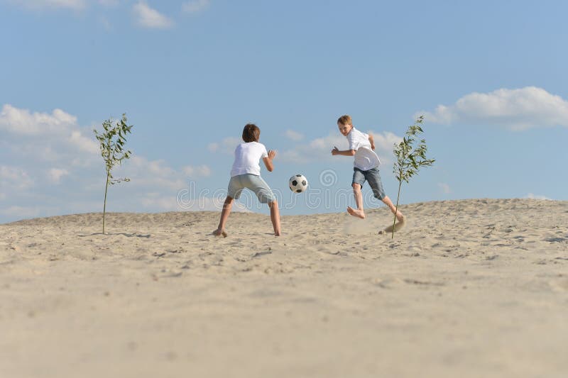 Broers die voetballen op het strand in de zomerdag