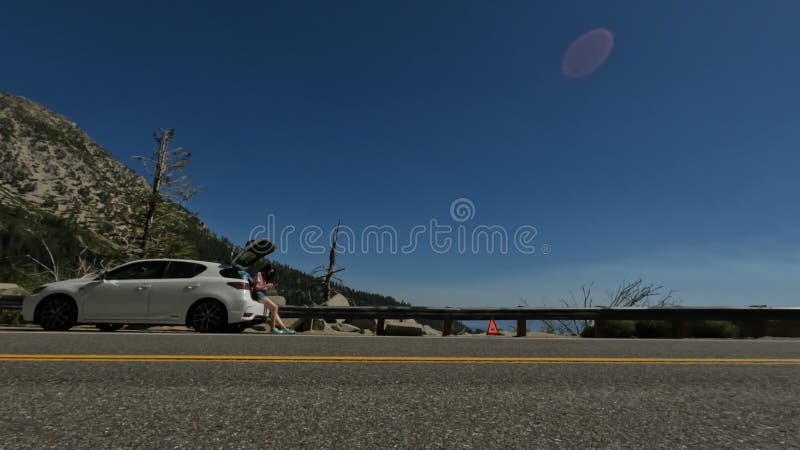 Broken Car on the Side of the Road with Emergency Triangle with Open Trunk and Female Waiting for Help Looking into a Phone with M