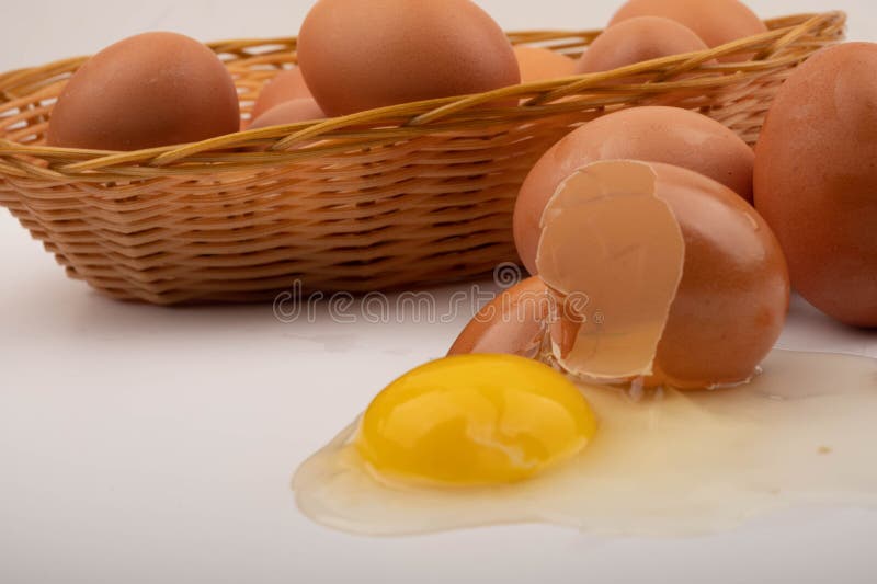 A broken chicken egg, chicken eggs in a wicker basket and chicken eggs scattered on a white background. Close up