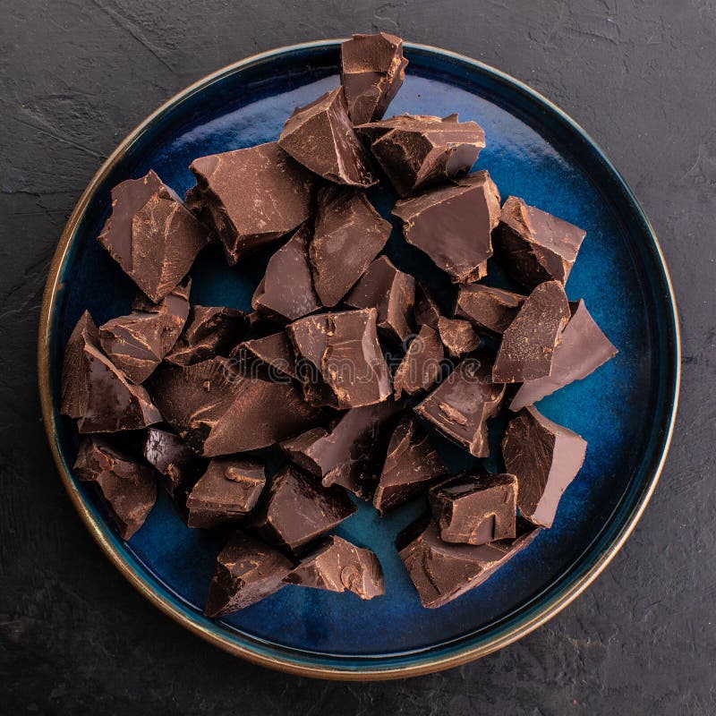 Broken Chocolate Pieces in a Blue Round Plate, Top View. Confectionery