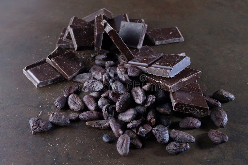 Broken dark chocolate and cocoa beans on a stone table close up stock afbeelding