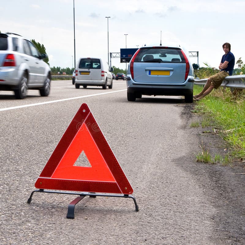 Man waiting outside of his broken car on the curb of a busy motorway with a warning triangle on the asphalt. Man waiting outside of his broken car on the curb of a busy motorway with a warning triangle on the asphalt