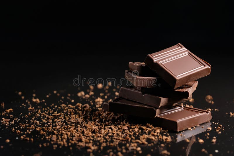 Broken pieces of chocolate with cocoa powder on a black background