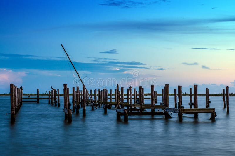 Broken pier and mast of broken ship in water after sunset