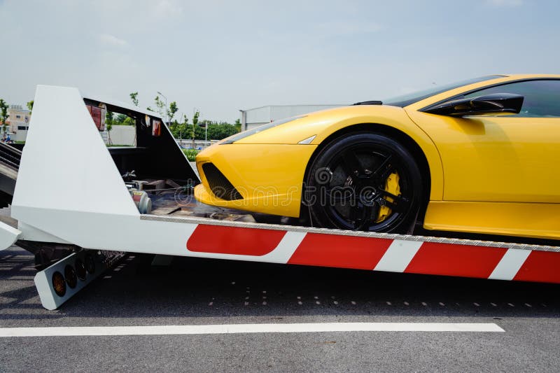 A broken vehicle strapped down to the platform of flat bed tow truck