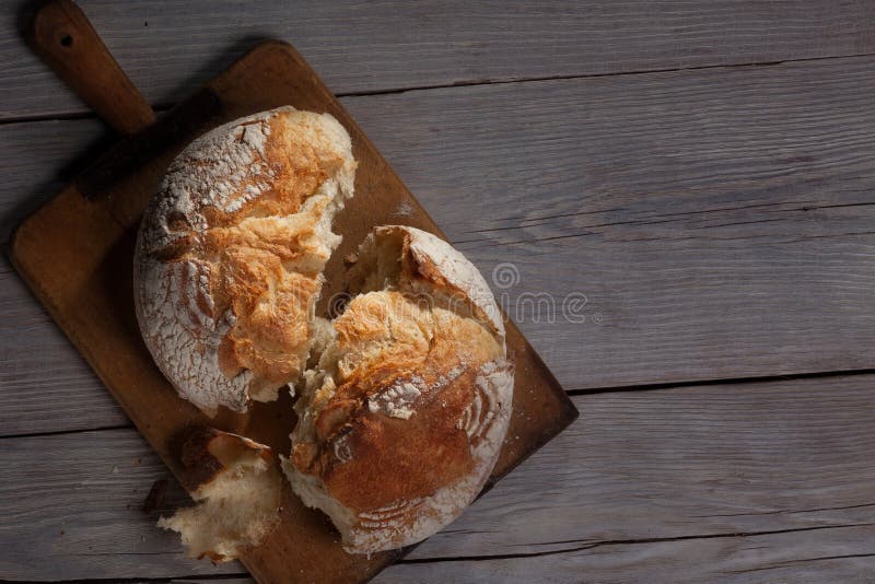 Torned crannied rustical homemade bread loaf on old cutting board over grey wooden table. Dark background with a free space. Torned crannied rustical homemade bread loaf on old cutting board over grey wooden table. Dark background with a free space.