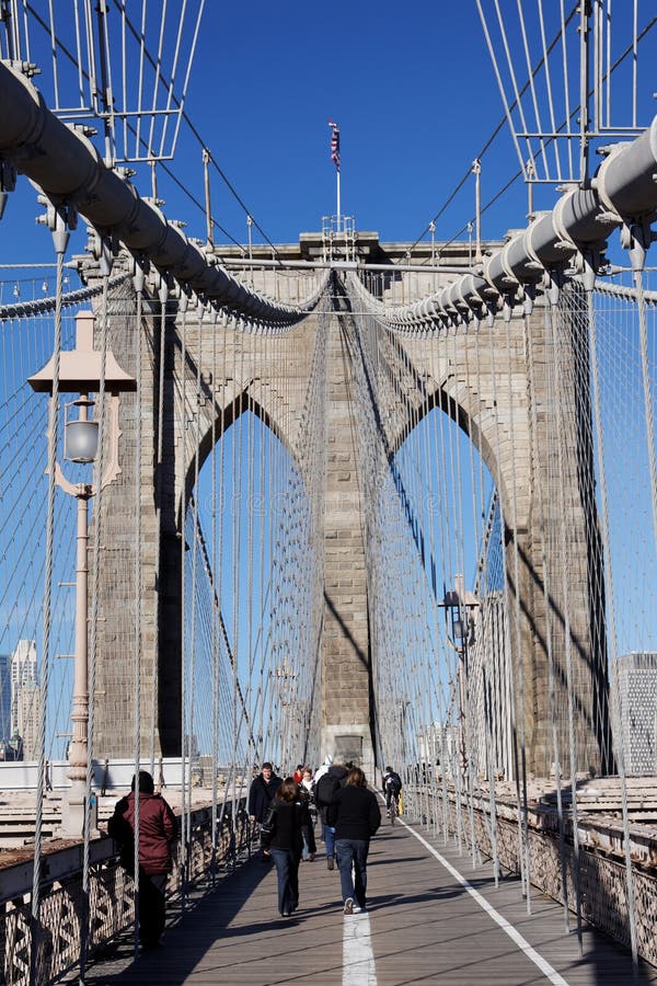Brooklyn Bridge. Tourists walking on Brooklin Bridge with its bricks, steel cables and an american flag. Manhattan Island, New York City, USA stock photos Brooklyn Bridge. Tourists walking on Brooklin Bridge with its bricks, steel cables and an american flag. Manhattan Island, New York City, USA stock photos