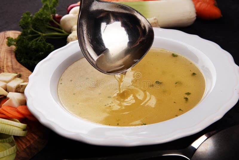 Broth with carrots, onions various fresh vegetables in a pot - colorful fresh clear spring soup. Rural kitchen scenery vegetarian