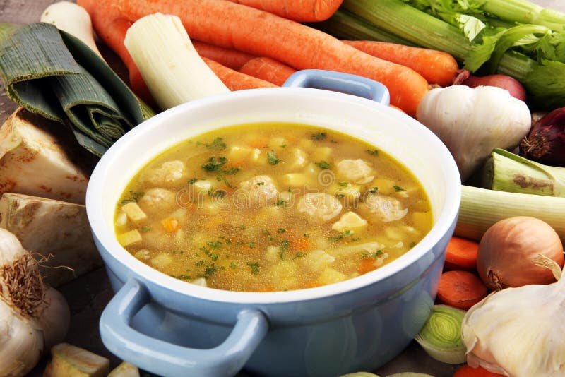 Broth with marrow dumplings and carrots, onions various fresh vegetables in a pot - colorful fresh clear spring soup. Rural