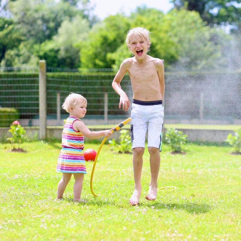Brother and sister playing with water hose in the garden stock photography Brother and sister playing with water hose in the garden stock photography