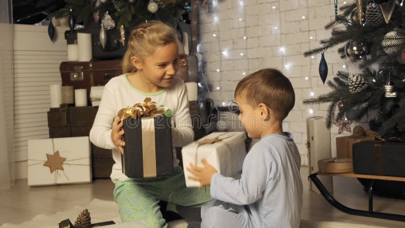 Brother and sister shake boxes with Christmas gifts under the Christmas tree in slow motion