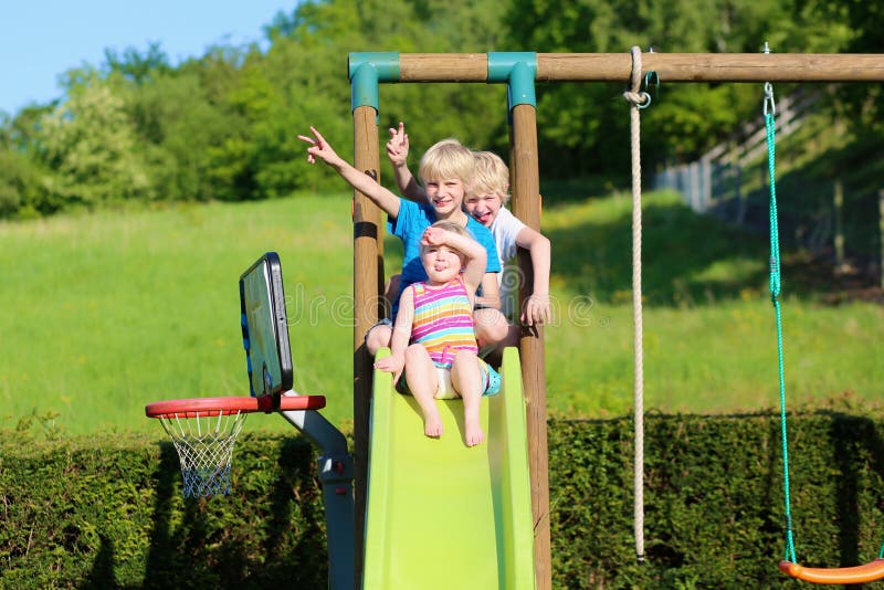 Brothers and sister playing on slide in the garden