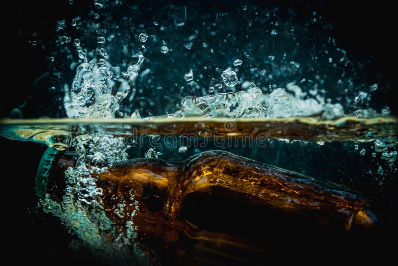 Brown beer bottle falls into water making big splash of drops and spray on a dark background. Juicy and fresh concept of