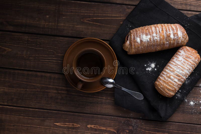 Brown filiżanka z herbatą i łyżkowa dwa babeczki z dżemem, rozpryskanym z mąki kłamstwem na czarnej pielusze br?zowe drewniane t? zdjęcie stock Brown filiżanka z herbatą i łyżkowa dwa babeczki z dżemem, rozpryskanym z mąki kłamstwem na czarnej pielusze br?zowe drewniane t? zdjęcie stock