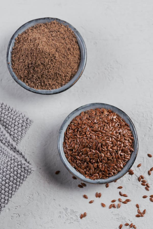 Brown flax seed and ground or crushed flaxseed or linseed in small bowl on light gray background royalty free stock image