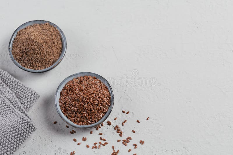 Brown flax seed and ground or crushed flaxseed or linseed in small bowl on light gray background stock photography