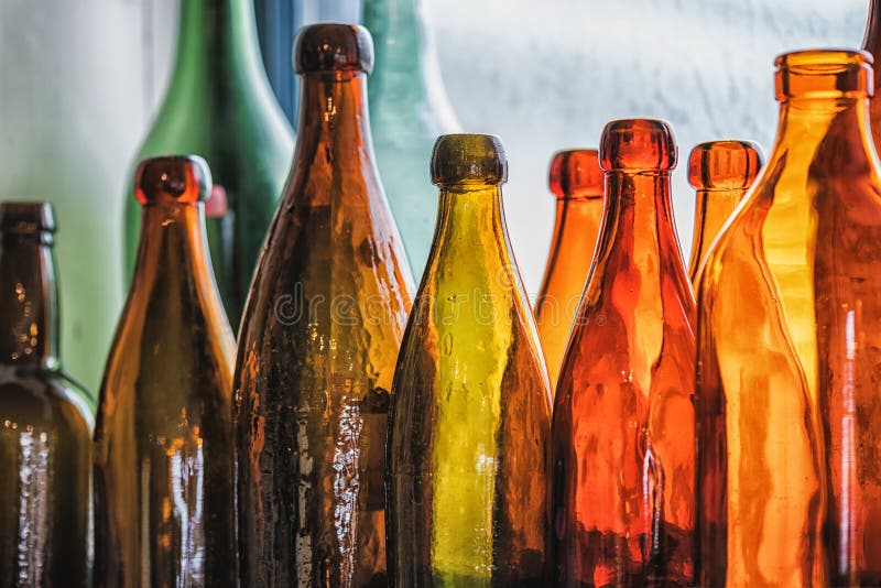 Brown and green old glass bottles on windowsill, with curtain. Closeup, daylight