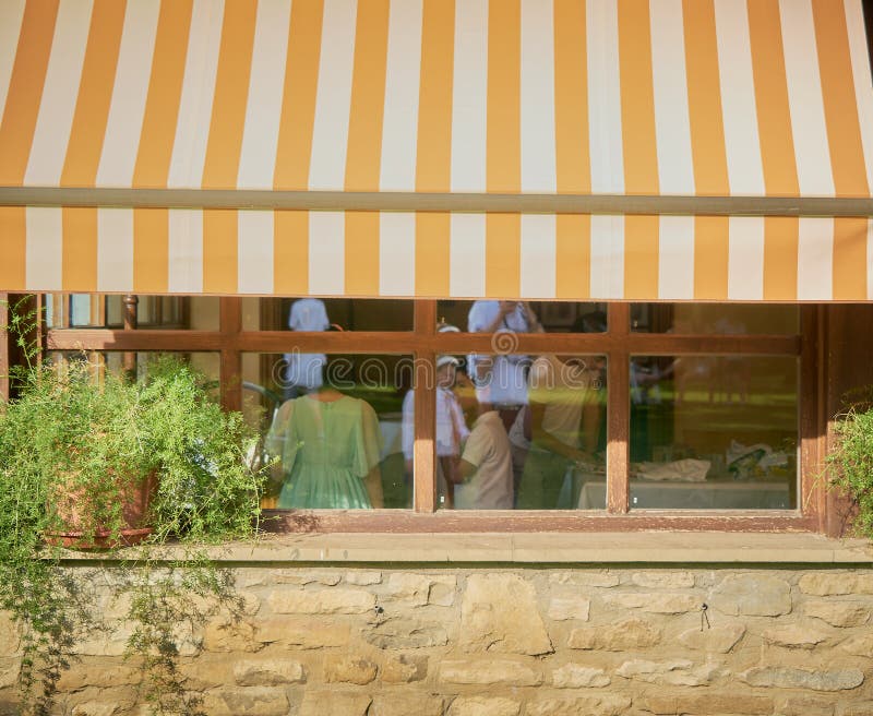 brown orange and white awning covering a window in a restaurant while unidentified people are inside