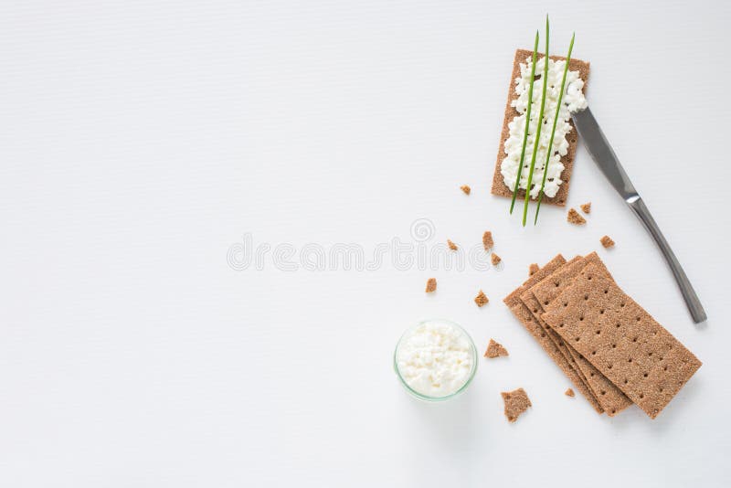 Brown rye crispy bread Swedish crackers with spread cottage cheese, decorated with thin green onion, on white background