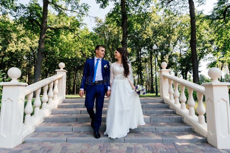 Bruden och brudgummen som går ner trappan i parkera Brudgummen omfamnar bruden Gifta sig par som är förälskade på wedddagen royaltyfria bilder Bruden och brudgummen som går ner trappan i parkera Brudgummen omfamnar bruden Gifta sig par som är förälskade på wedddagen royaltyfria bilder