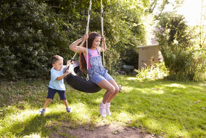 Bruder-Pushing Sister On-Reifen-Schwingen im Garten lizenzfreie stockfotografie Bruder-Pushing Sister On-Reifen-Schwingen im Garten lizenzfreie stockfotografie