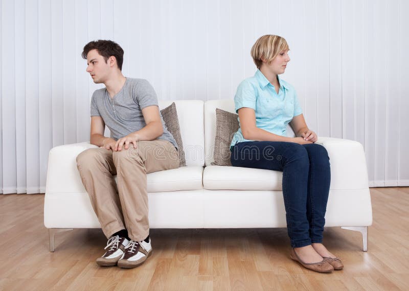 Brother and sister have had an argument and are sitting at opposite ends of a sofa. Brother and sister have had an argument and are sitting at opposite ends of a sofa