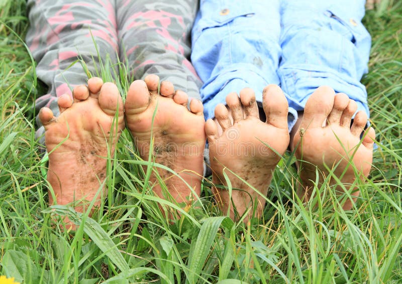 Dirty soles of bare feet of two little girls - kids sitting on green grass. Dirty soles of bare feet of two little girls - kids sitting on green grass