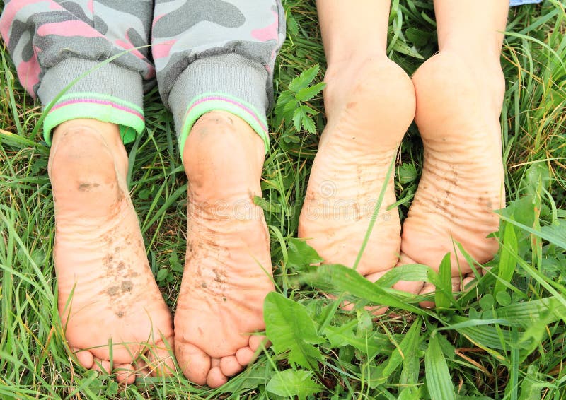 Four dirty soles of bare feet of two little girls - kids lying on green grass. Four dirty soles of bare feet of two little girls - kids lying on green grass