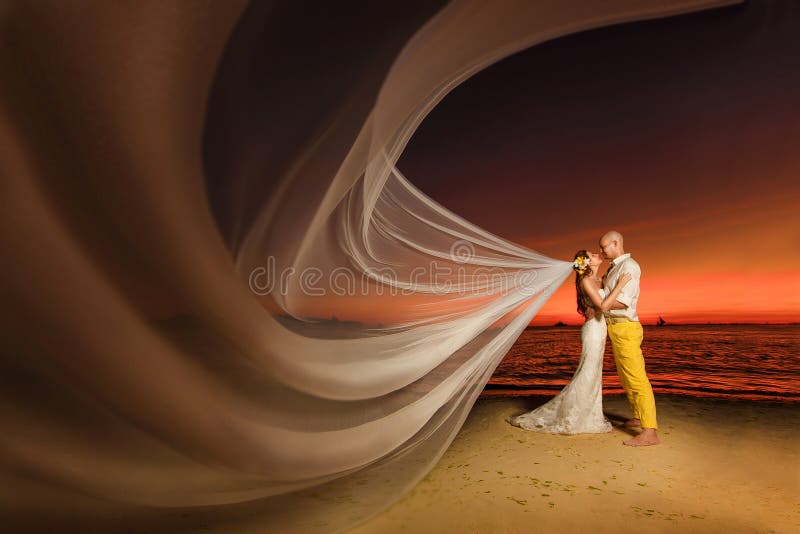 Bruid en bruidegom op een tropisch strand met de zonsondergang in backg stock afbeelding Bruid en bruidegom op een tropisch strand met de zonsondergang in backg stock afbeelding
