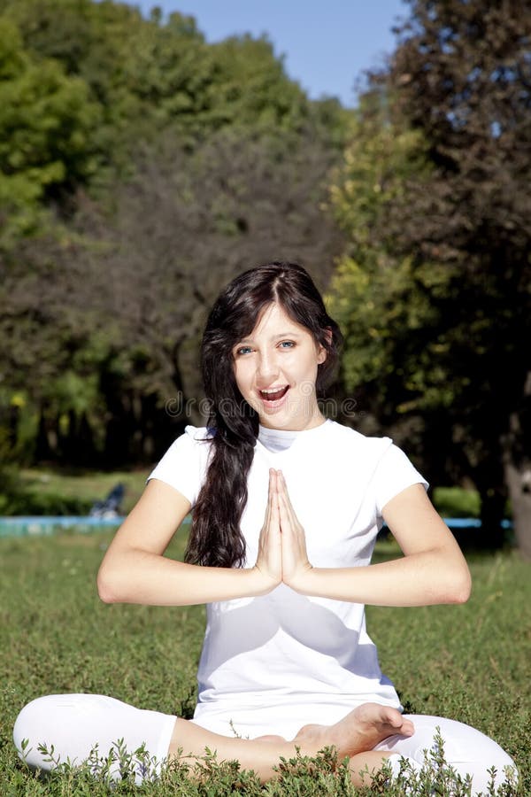 Brunet yoga girl on green grass in park.