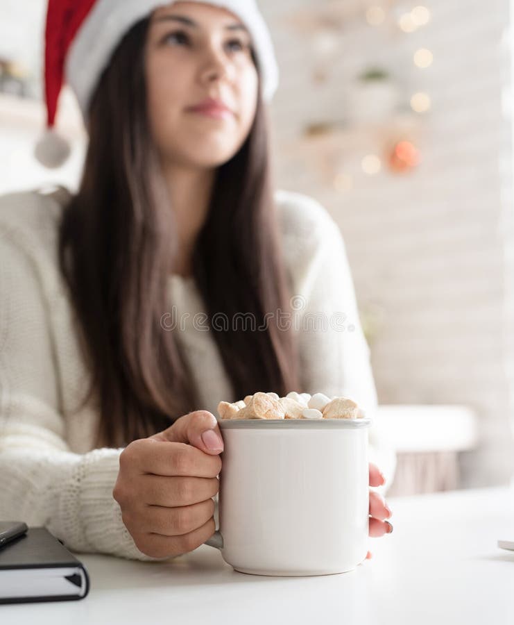 Brunetka w kapeluszu santa trzymająca filiżankę piankowego kakao zdjęcie stock