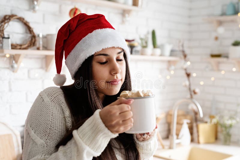Brunetka w kapeluszu santa trzymająca filiżankę piankowego kakao w kuchni zdjęcie royalty free