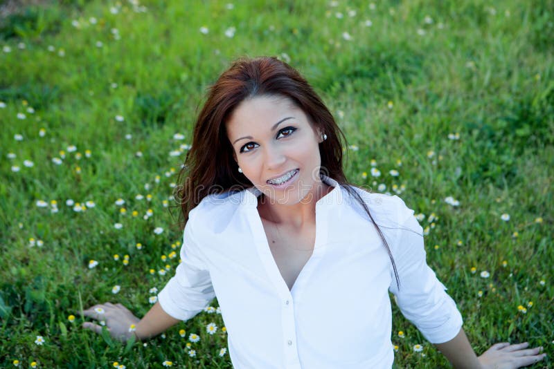 Brunetki dziewczyna siedzi na trawie z wiele daisi z wspornikami fotografia stock