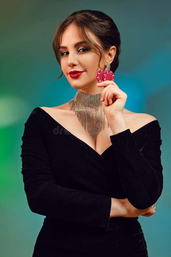 Brunette female in black dress, necklace and earrings. She is smiling, showing two red chips, posing on colorful