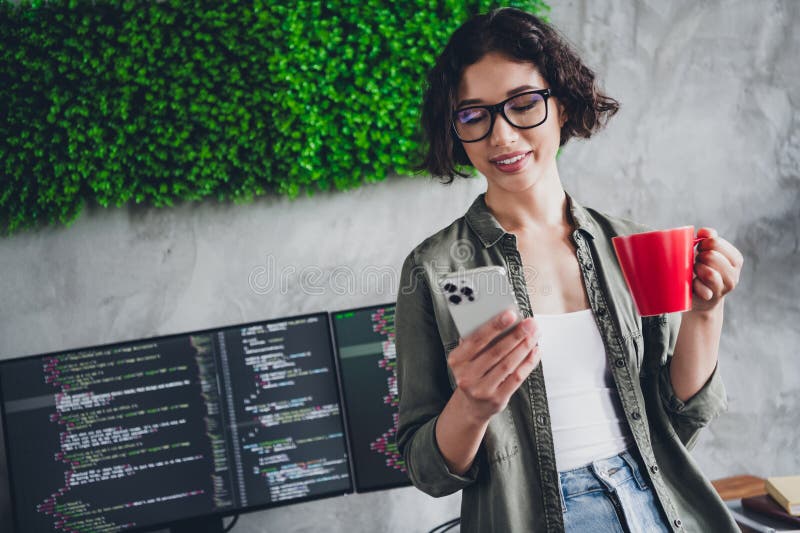 Brunette Female Programmer Working Remotely with a Smartphone and Coffee in a Modern Workspace with Computer Monitors stock photography