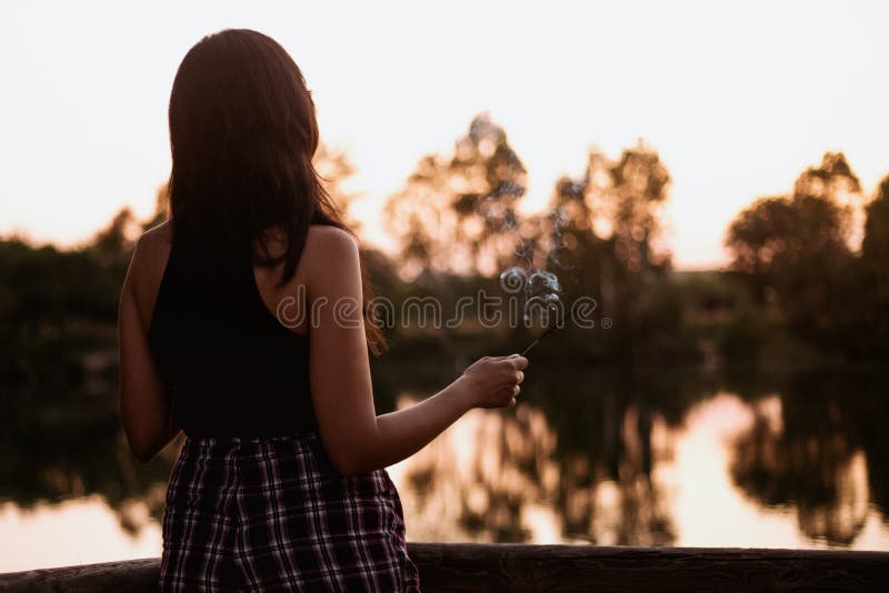 Brunette woman at sunset on a lake with an incense stick a summer day. Brunette woman at sunset on a lake with an incense stick a summer day