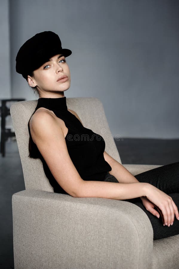 Brunette girl in black with cap posed at studio on chair royalty free stock photo Brunette girl in black with cap posed at studio on chair royalty free stock photo