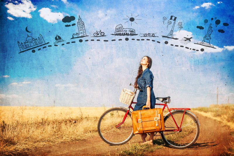 Brunette girl with bycicle and suitcase on country side road.