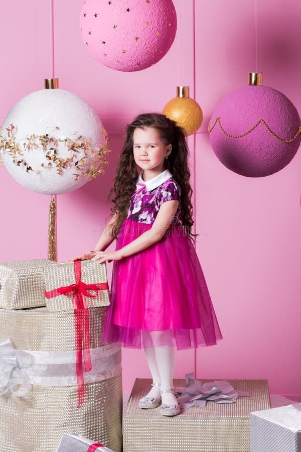 Brunette girl child 5 years old in a pink dress. in holiday rose quartz room with gifts.