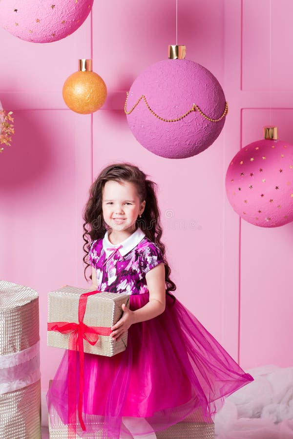 Brunette girl child 5 years old in a pink dress. in holiday rose quartz room with gifts.