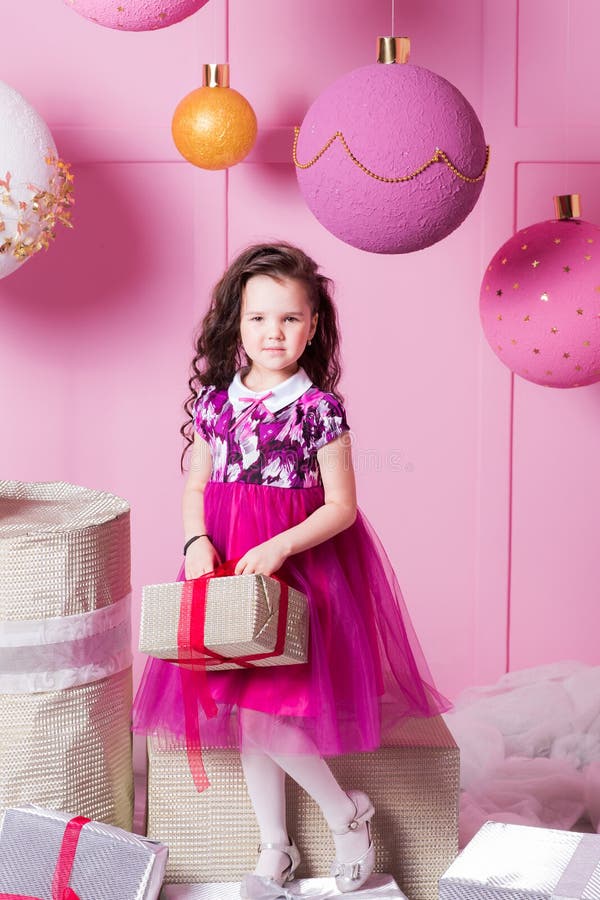 Brunette girl child 5 years old in a pink dress. in holiday rose quartz room with gifts.