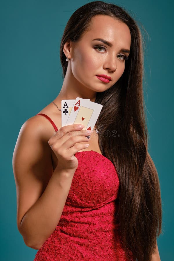 Brunette girl with a long hair, wearing a sexy red dress is posing holding two playing cards in her hand, blue