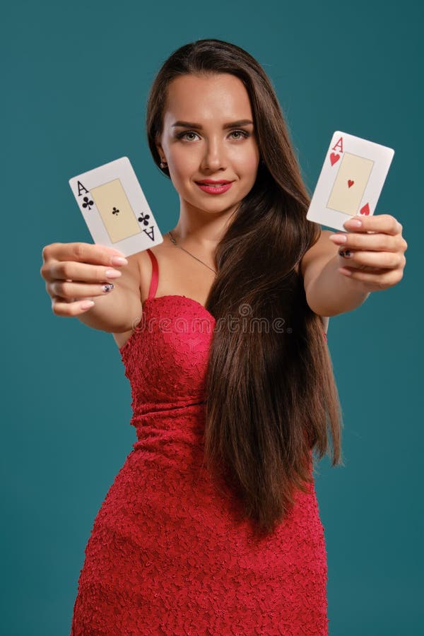 Brunette girl with a long hair, wearing a sexy red dress is posing holding two playing cards in her hands, blue