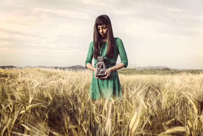 Brunette girl with retro camera in meadow