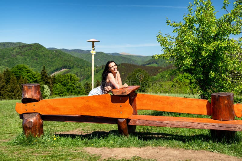 Brunetka sedící na dřevěné lavici v krásné letní zemi